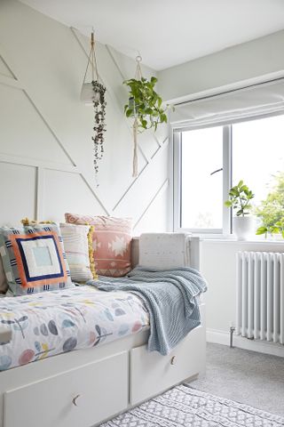 Spare room with white geometric panelled walls, white daybed and floral bedding, and multicolour cushions