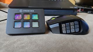 A Corsair Scimitar Elite Wireless SE gaming mouse on a carpet next to a gaming laptop and Stream Deck.