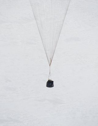 Close-up of the Soyuz TMA-16 spacecraft returning from the International Space Station showing the bell-shaped descent module dangling beneath the main parachute over Kazakhstan in Central Asia.