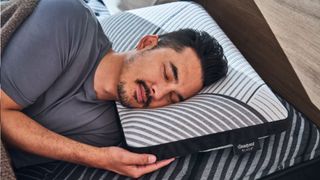 The image shows a man sleeping on the Beautyrest Black Luxury Foam Pillow