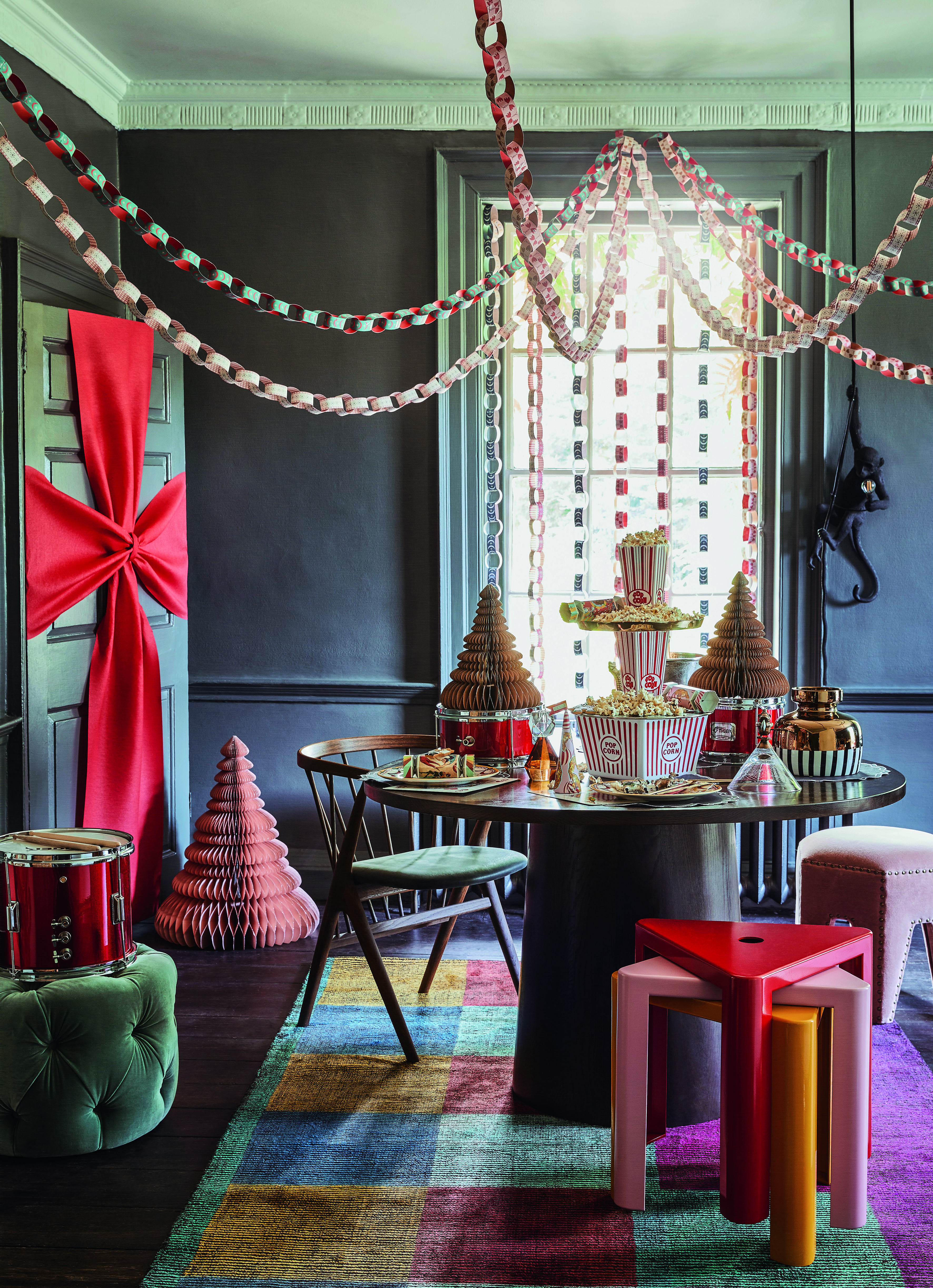 A Christmas dining room with paper streamers hanging above the table fanning out to the corners of the room, and the door is decorated with a giant bow while paper christmas trees sit on the floor and table