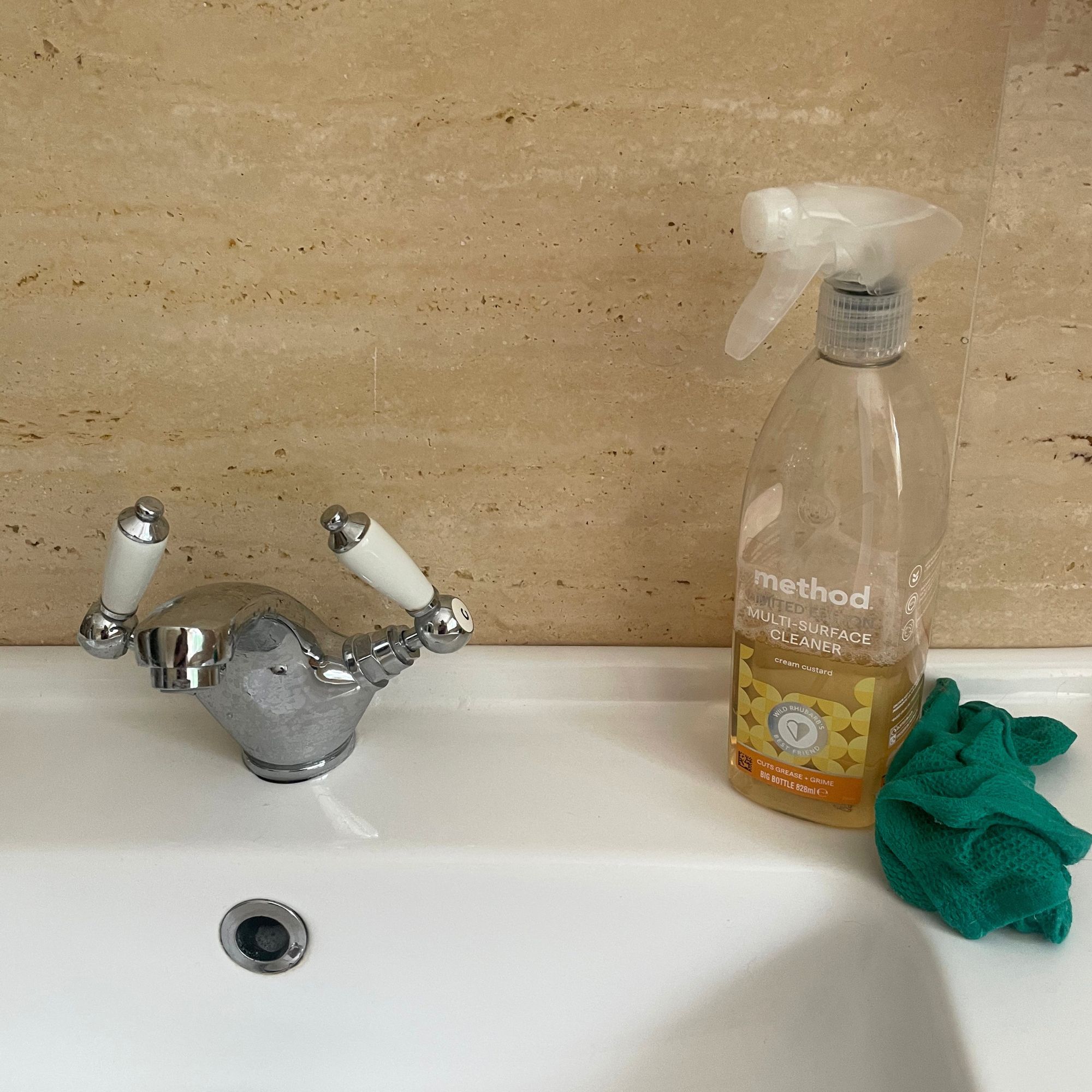 Cleaning bottle sitting on a white sink, next to a green cleaning cloth