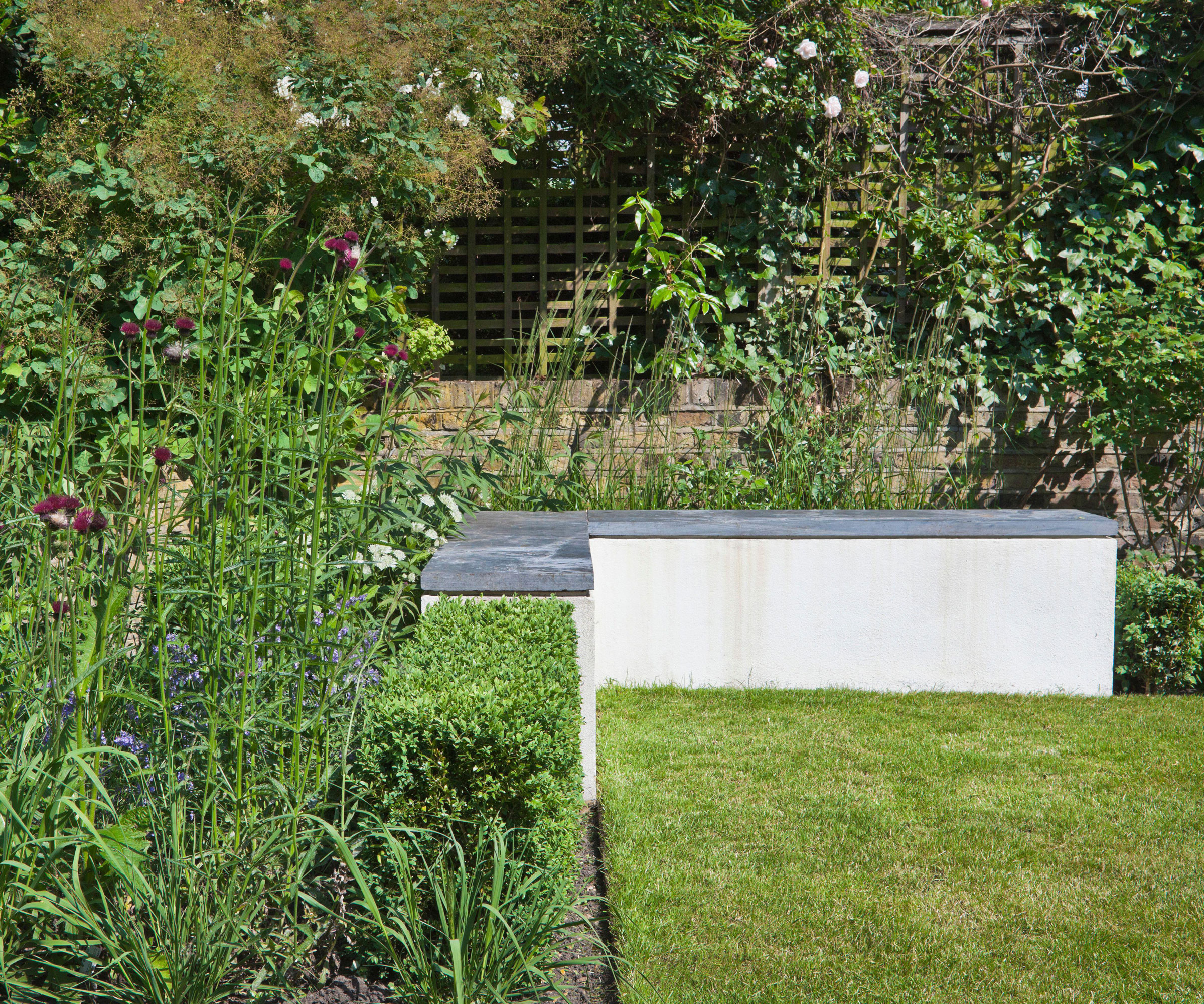 concrete L-shaped garden bench with lawn and flower beds