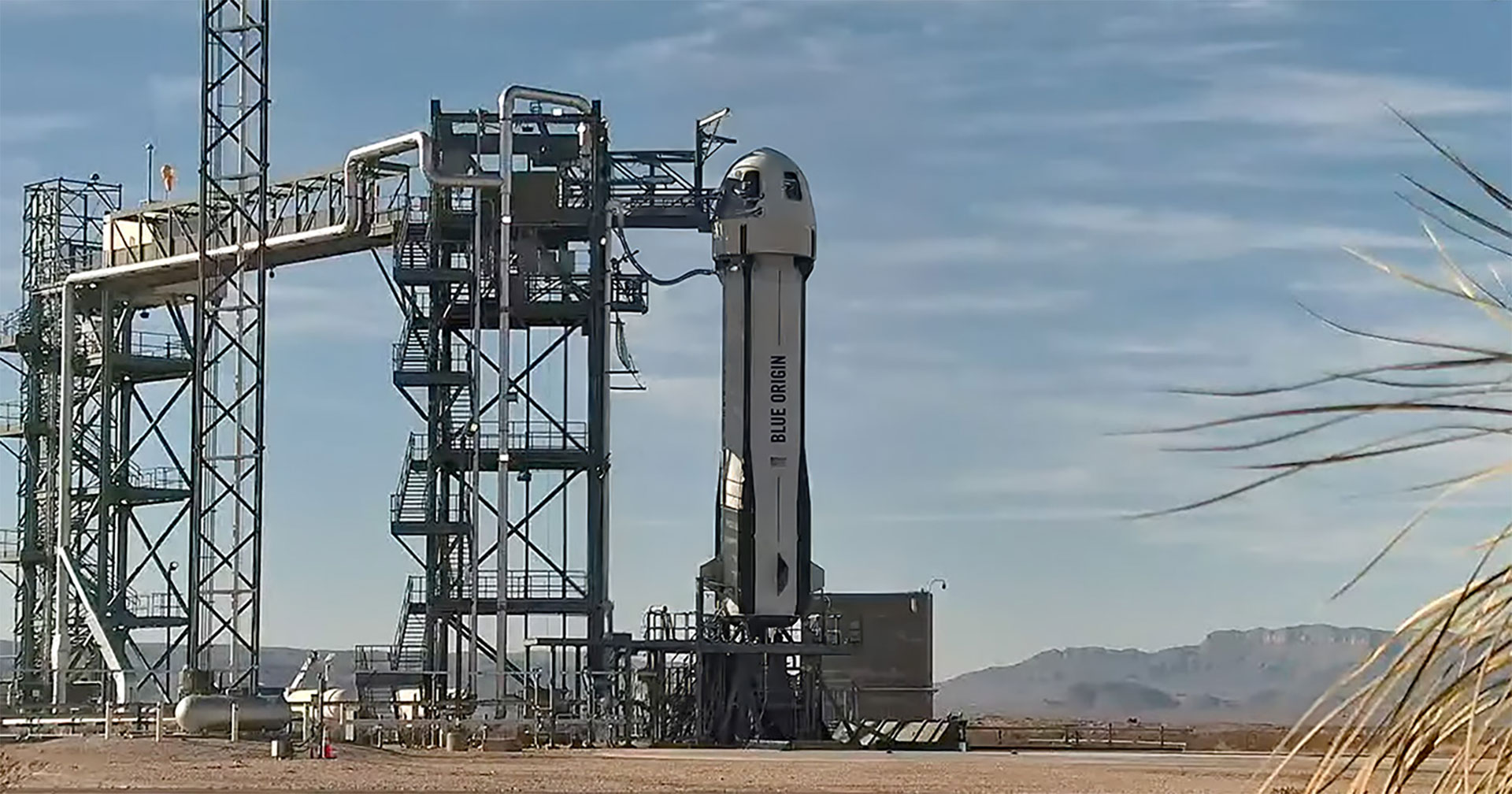 a white rocket topped by a gumdrop-shape capsule sits on its launch pad in a mountain valley.