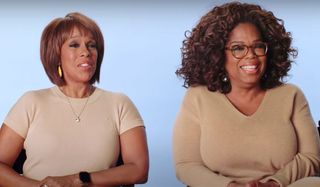 Oprah Winfrey and Gayle King laugh and sit next to each other in chairs during an interview.
