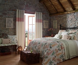 bedroom with stone interior walls and wooden vaulted ceiling, small patio doors and floral soft furnishings