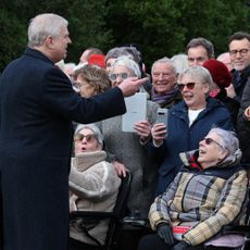 Prince Andrew wearing a long coat talking to a crowd of royal fans who are smiling and taking his photo on Christmas Day