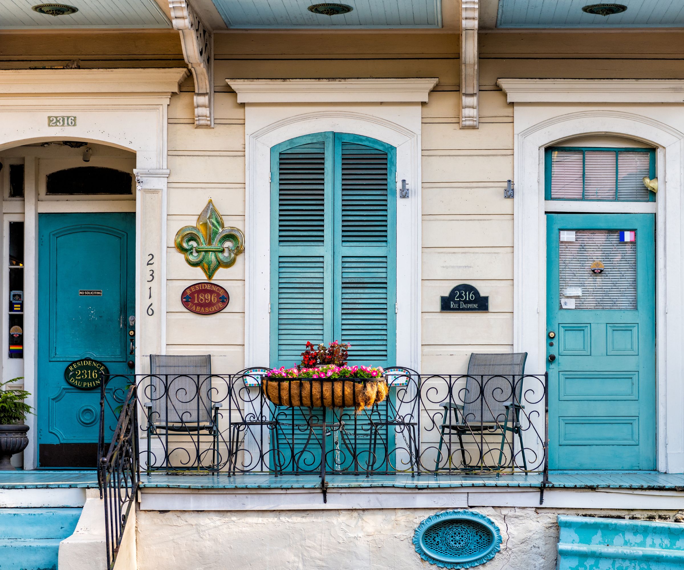 Shotgun house facade with blue shutters and doors, iron railing and potted plant