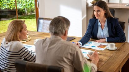 An adviser smiles as she meets with an older couple at their dining room table.