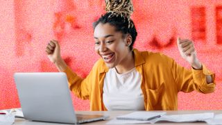 Young woman sitting at a computer desk looking excited in front of laptop.