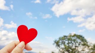 A hand holding a red love heart up to the sky