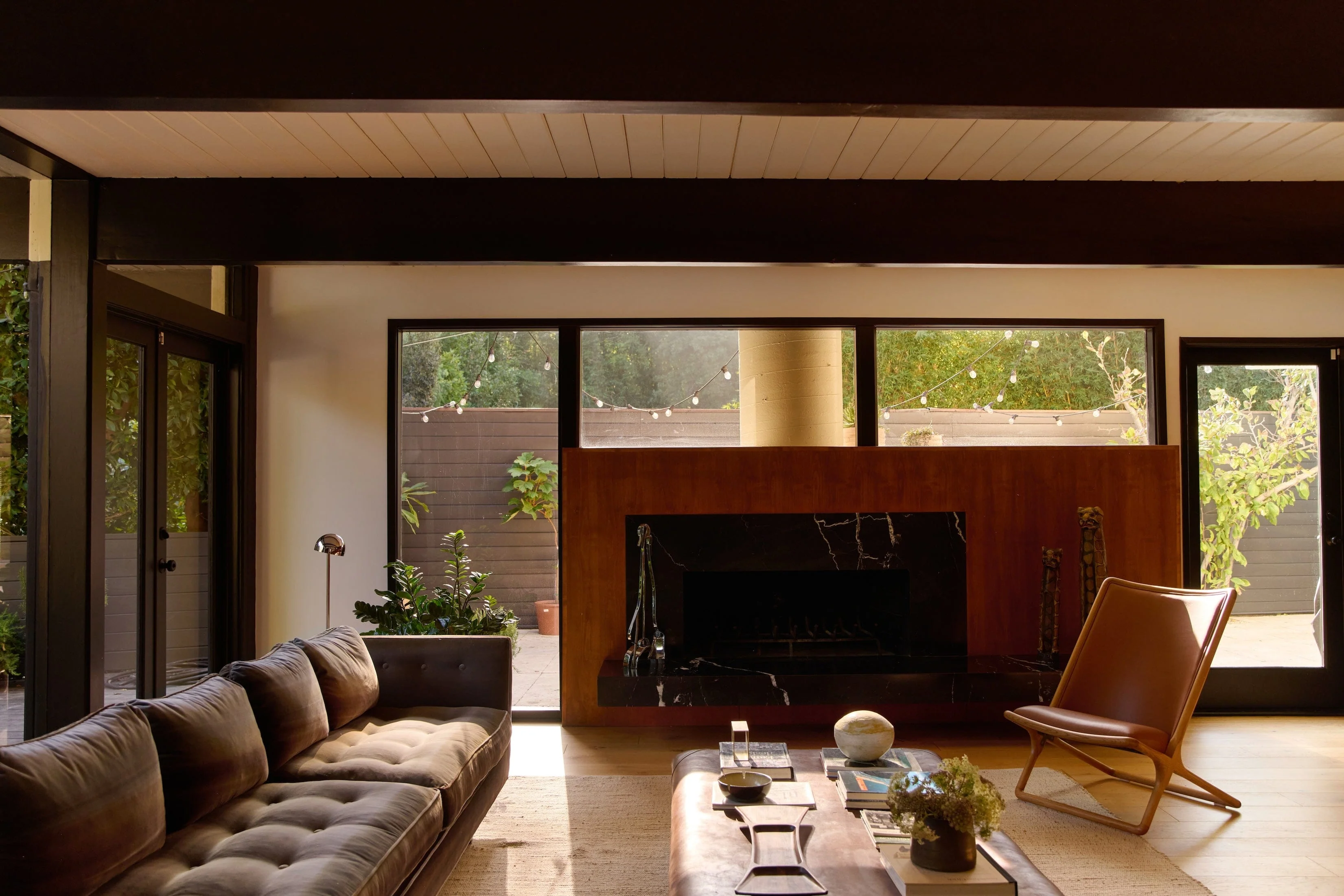 troye sivan's hollywood hills home living room with built-in marble fireplace, paneled ceiling, picture windows, a large sofa, herman miller scissor chair and coffee table