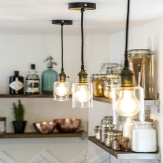 Three pendant lights suspended from a ceiling with two wooden shelves in the background