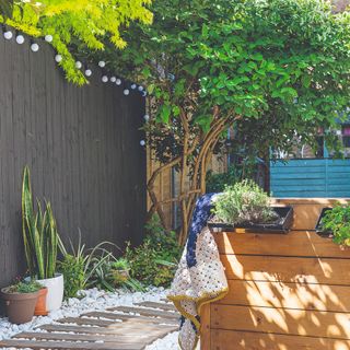 small garden with black wooden fence boardwalk on white gravel and wooden outdoor seating