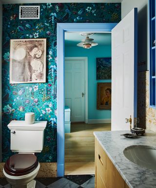 bathroom with teal floral wallpaper, light blue doorframe, marble countertops and artwork on wall