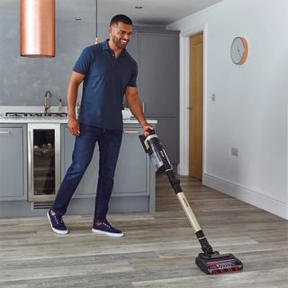 A person using a Shark cordless vacuum on a wooden floor