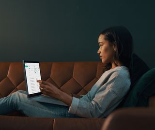 A woman stretched out on a sofa working on a laptop