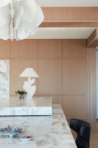 A marble kitchen with a white lamp on top and a small plant. Above the island is a unique, flower like white pendant