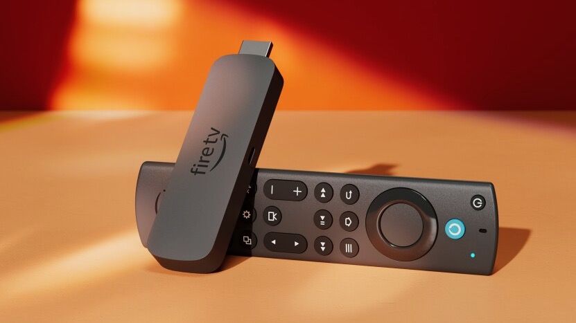 The Amazon Fire TV Stick 4K (2023) propped up on its Alexa remote control on a sun-dappled surface.