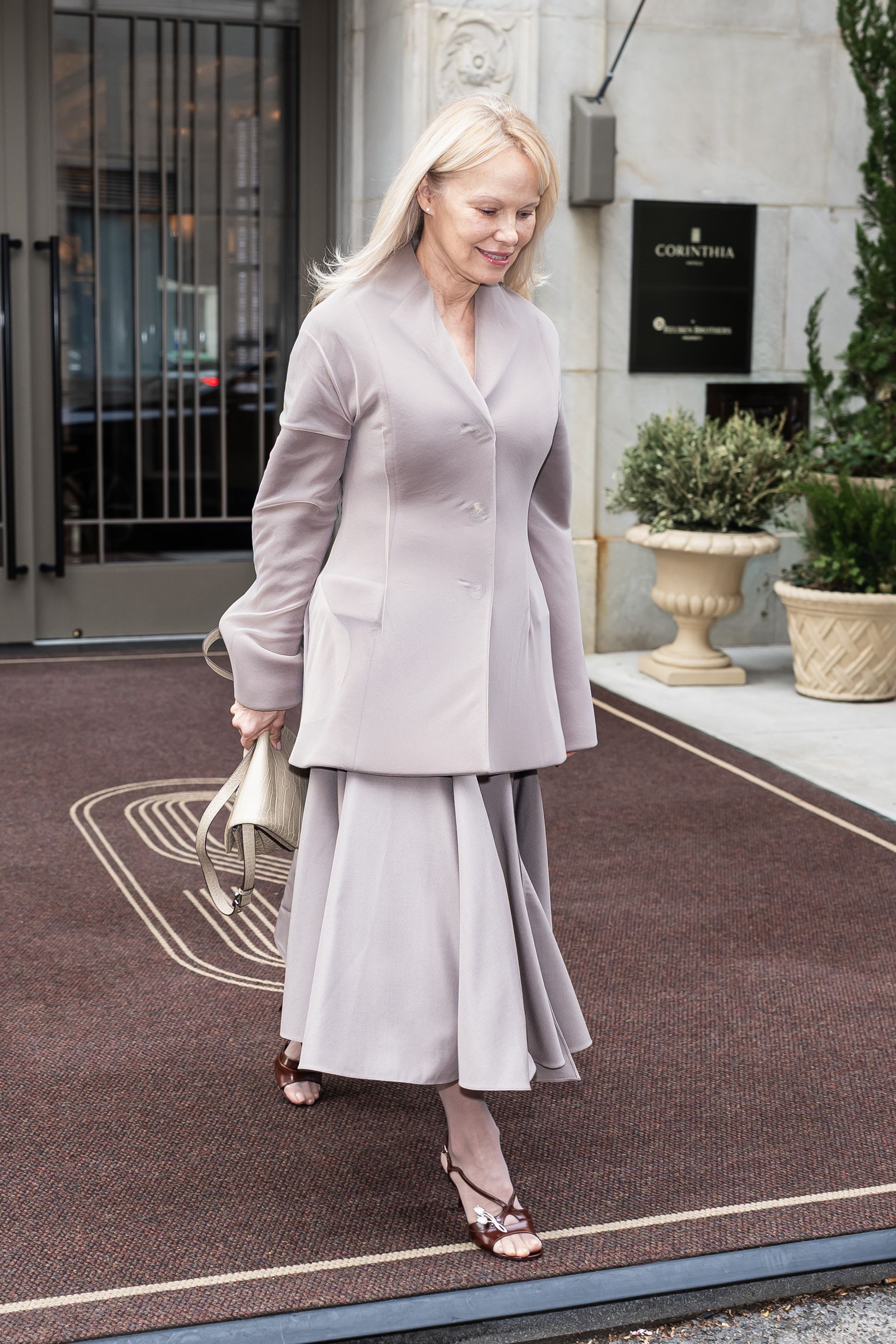 Pamela Anderson steps outside wearing tights with open-toe sandals and a knee-length skirt.