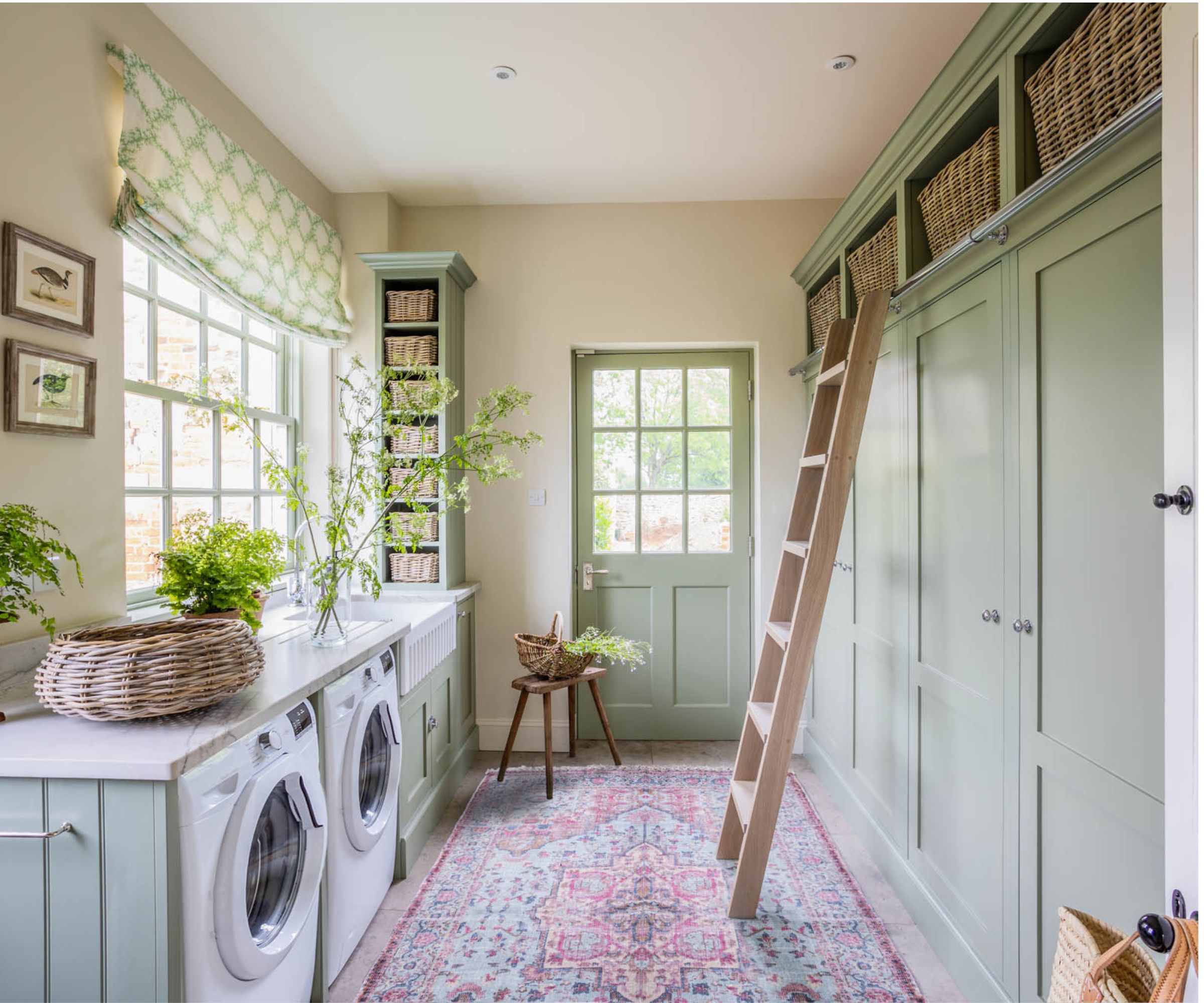 Country style laundry room by Sean Symington with sage green floor to ceiling cabinets, vintage rug and fabric roman blind, photograph Chris Wakefield