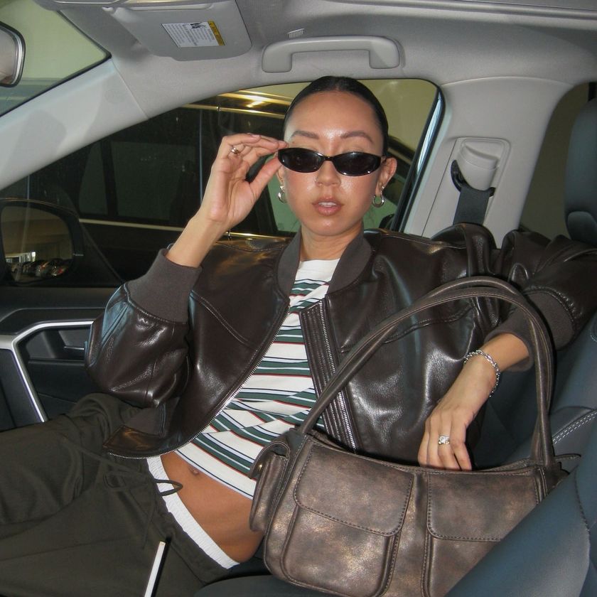 A woman wearing a brown leather jacket, striped shirt, brown pants, and brown leather bag