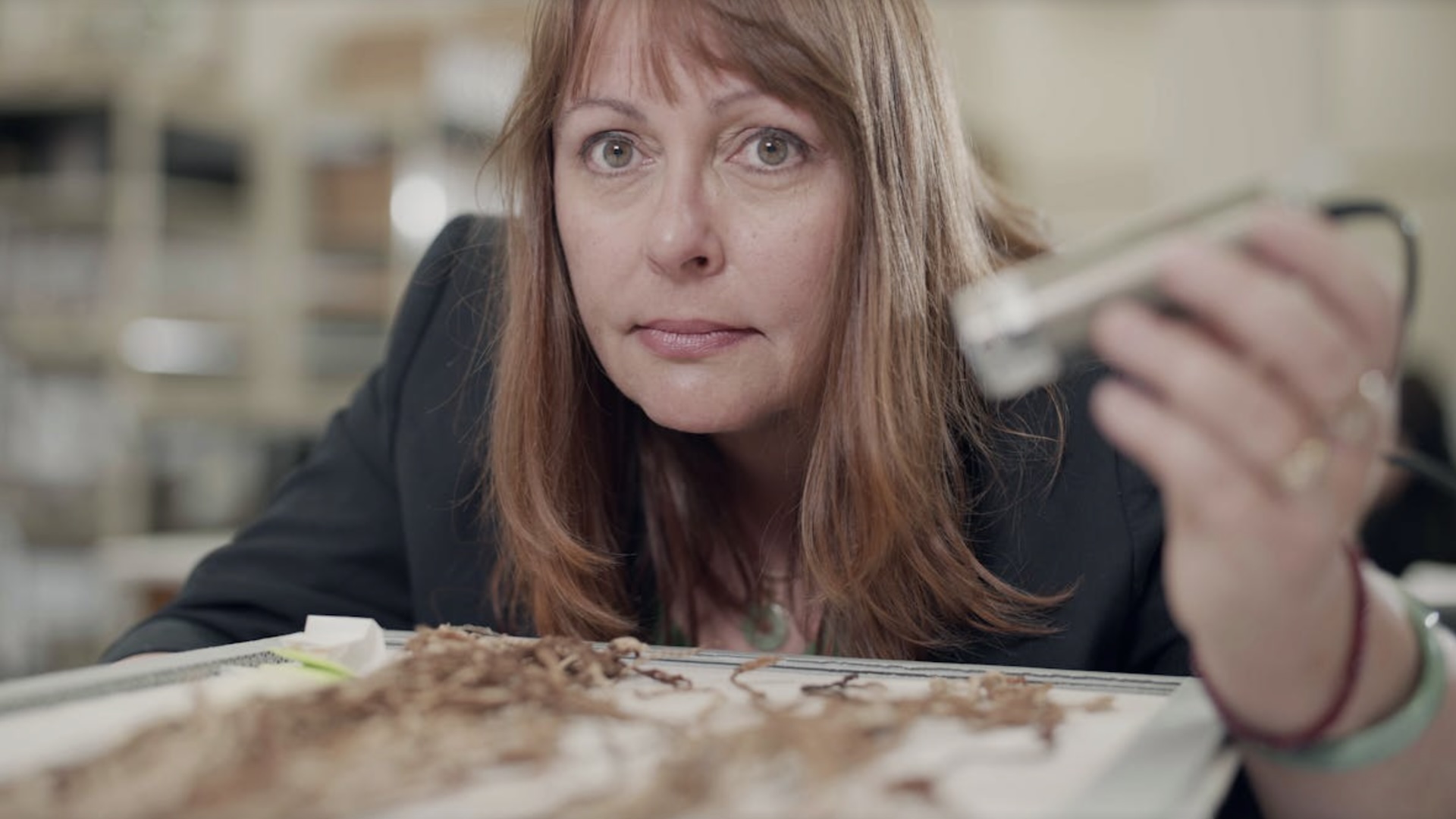 Sabine Hyland leans over a tray of frayed knotted strings holding a light