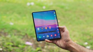 Ein Samsung Galaxy Z Fold 3 in der Hand von jemandem, im Hintergrund ist eine Wiese zu sehen