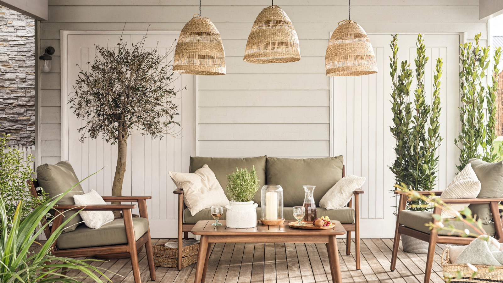 Garden area with sofa, olive trees, rattan lights and wooden decking under a cover