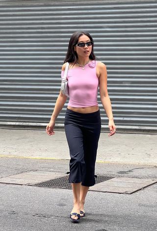 a woman wearing capri pants with a pink top and black mules