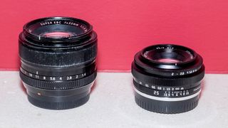 The TTArtisan 25mm f/2 lens and Fujifilm XF 35mm f/1.4 lenses on a stone shelf with red wall behind it
