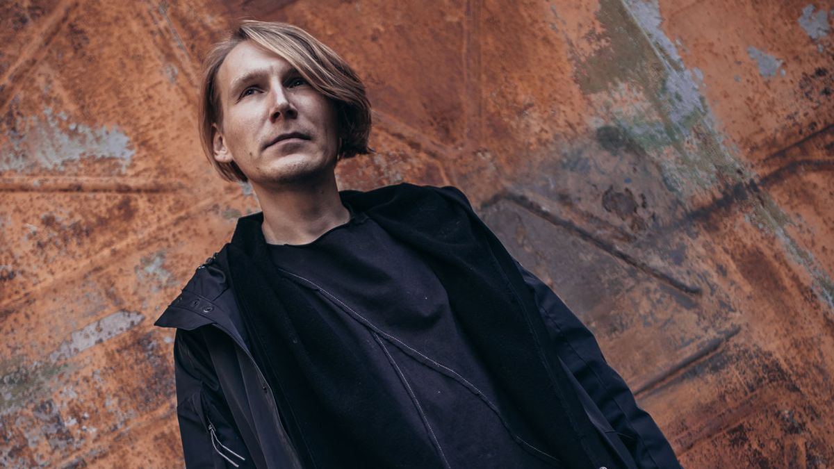 Gleb Kolyadin is dressed in black and stands in front of a brick wall