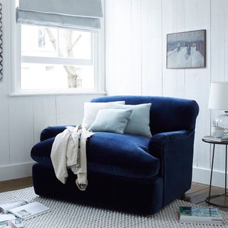 A blue velvet chair bed by a living room window