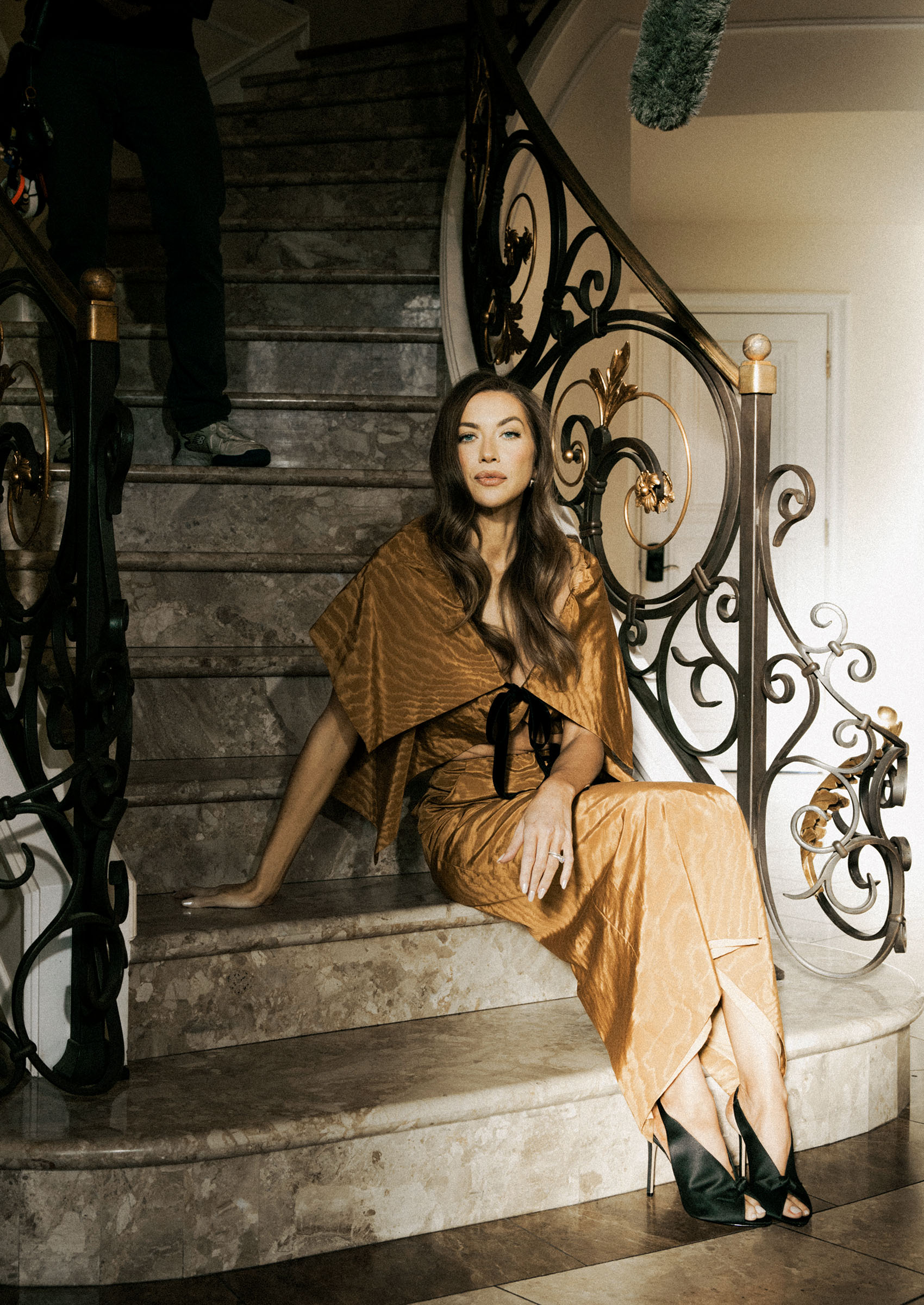 stassi schroeder wears a brown silk dress and shawl as she poses sitting on marble steps in an editorial shoot