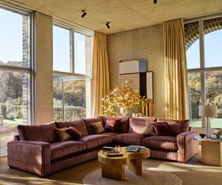 purple patterned large corner sofa in a large industrial living room with yellow curtains and a wooden coffee table