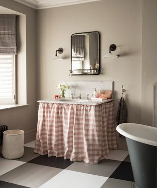 A traditional bathroom with large black and white checkered flooring and a pink and white gingham curtain below the sink