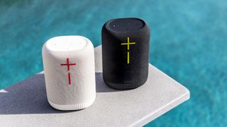 Two UE Epicboom speakers on a diving boards, with the azure pool in the background