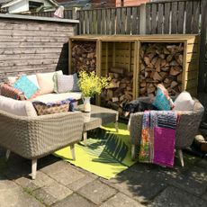 Outdoor sofa and armchairs with colourful cushions and throws around coffee table on top of bright coloured rug