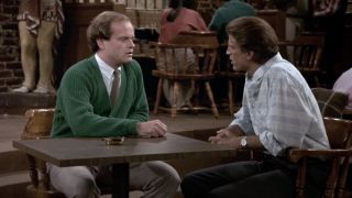 Frasier and Sam at a table speaking to each other in Cheers