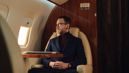 Young Elegant Confident Male Businessman with eyeglasses in a blue jacket looking through a corporate jet window