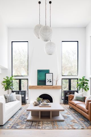 white living room with high ceiling, large windows, fire place, two couches opposite each other, large coffee table, rug, trio of statement pendants