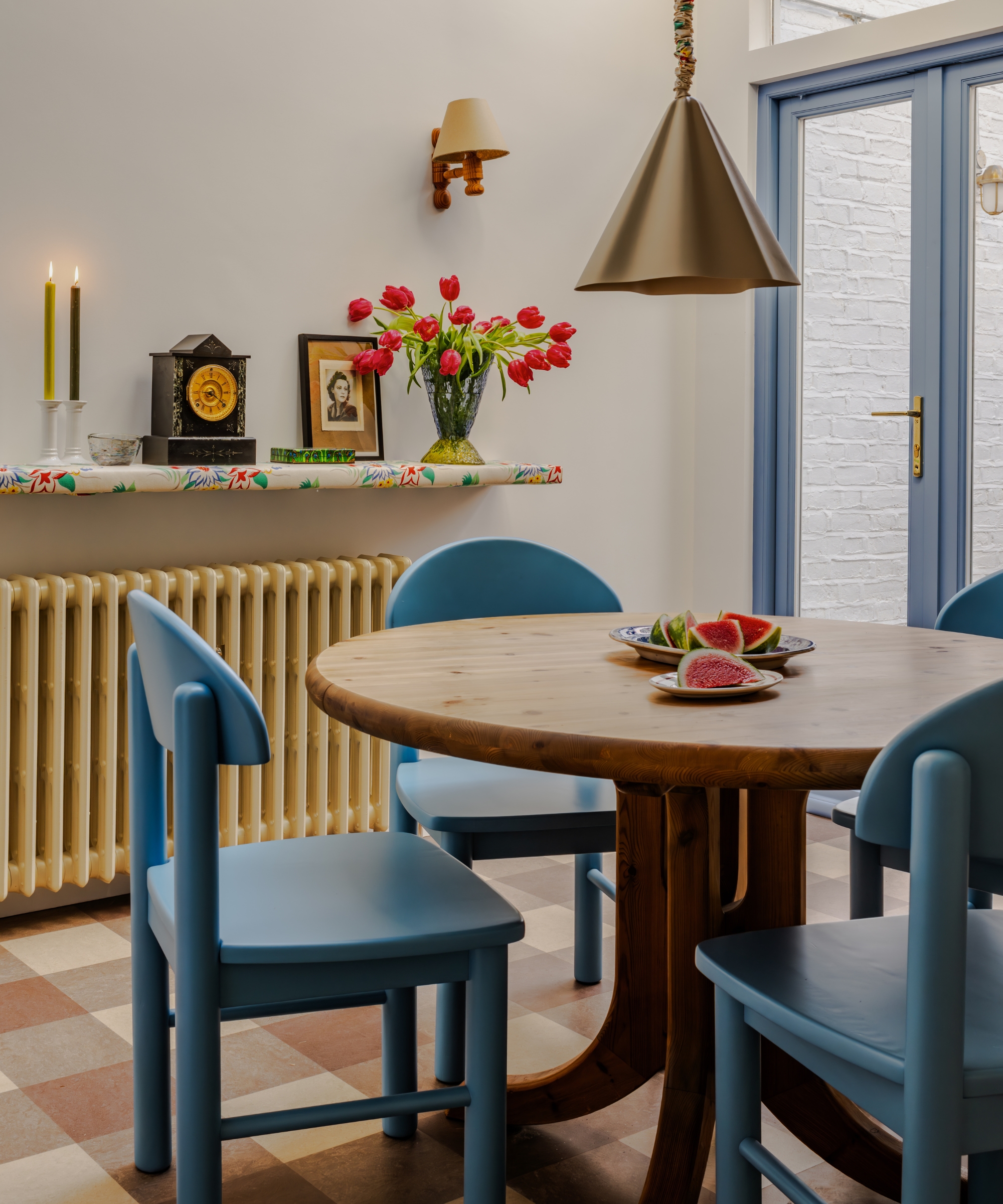 A small dining room with white walls, blue door frames, a round wooden table, blue chairs and gingham floor tiles