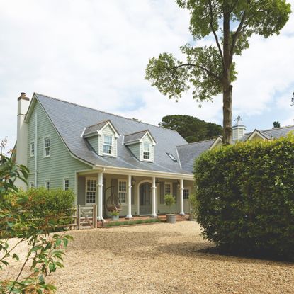 exterior of hamptons-style clapboard house with covered porch with pillars, dormer windows and pale green exterior