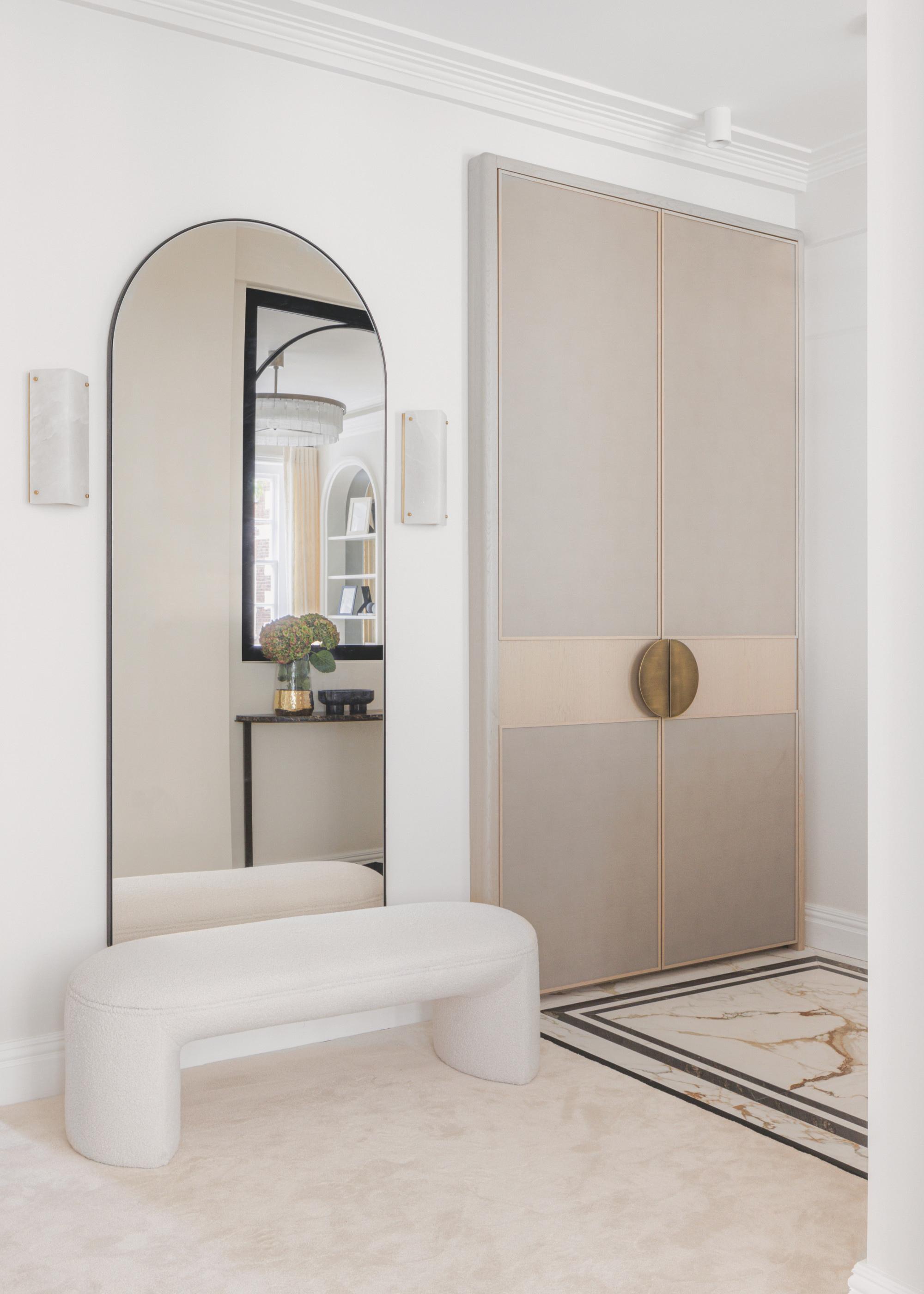 A large rounded mirror set above a small cream bench.