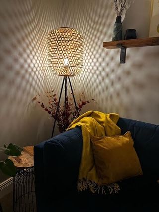 a corner of a snug with a rattan floor lamp switched on casting patterns on the corner walls with a yellow throw draped over a navy blue sofa