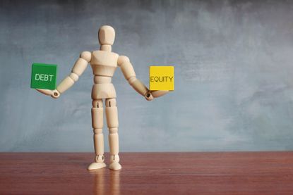 Debt and equity balance concept. Wooden human figure balancing wooden cubes with text DEBT and EQUITY.