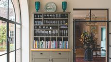 Olive green dresser stacked with glassware and books, in a dining room with Crittall windows