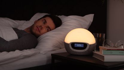 Man lying in bed looking at Lumie Bodyclock Shine 300 wake up light, which is on dim