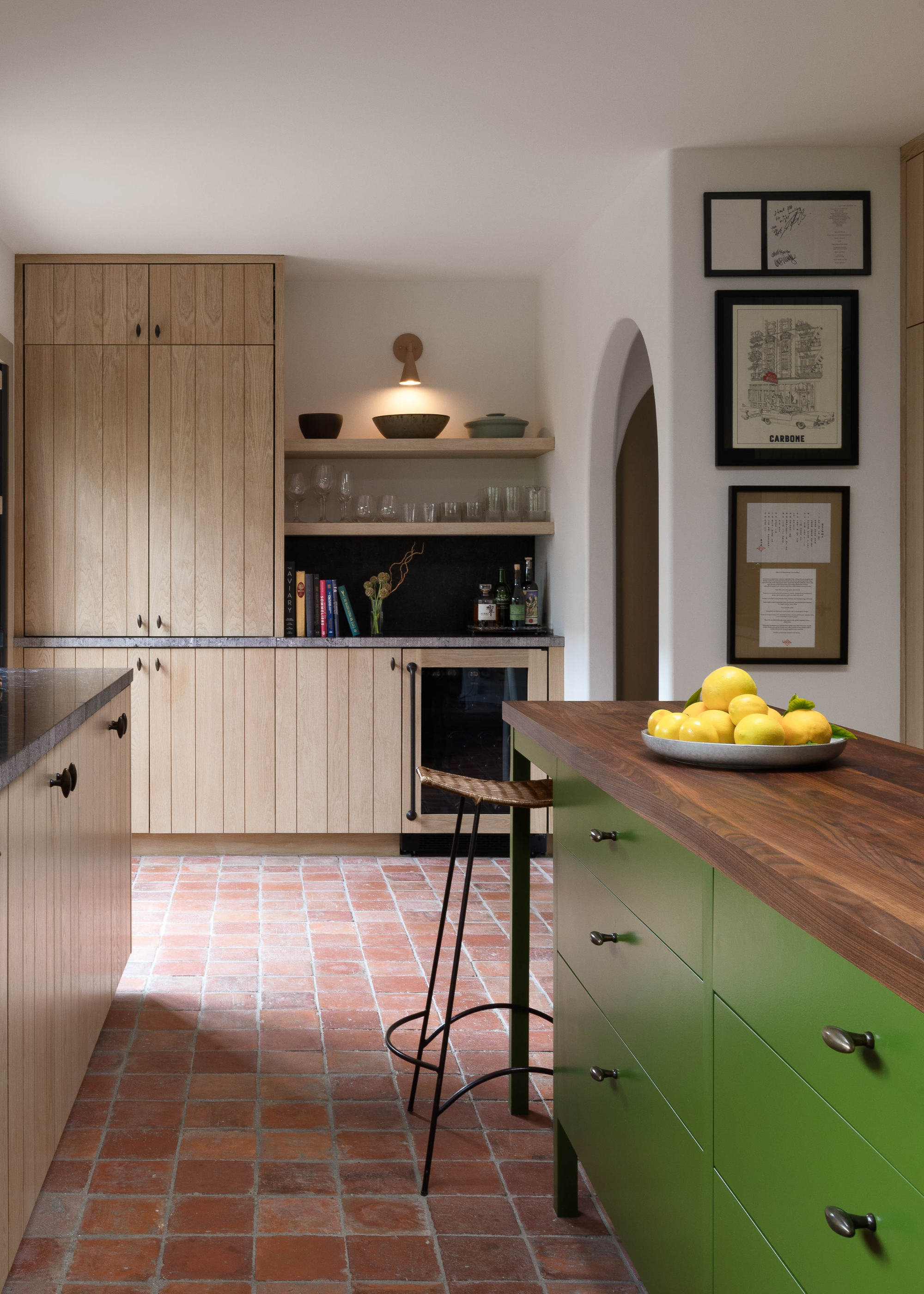 A light wood panelled kitchen with an apple green island and dark wood on top, all sitting on a teracotta floor