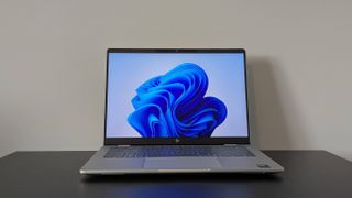 Front view of HP OmniBook 7 14-inch open on black desk with white wall in background